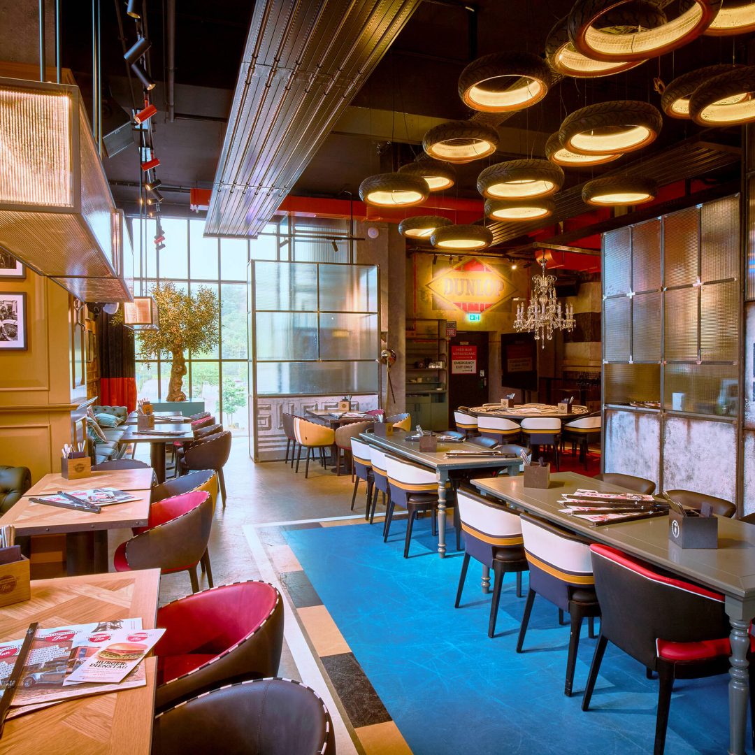 Stylisches Restaurant im Industrial-Look mit bunten Stühlen, Autoreifen-Lampen und Vintage-Werbeschildern