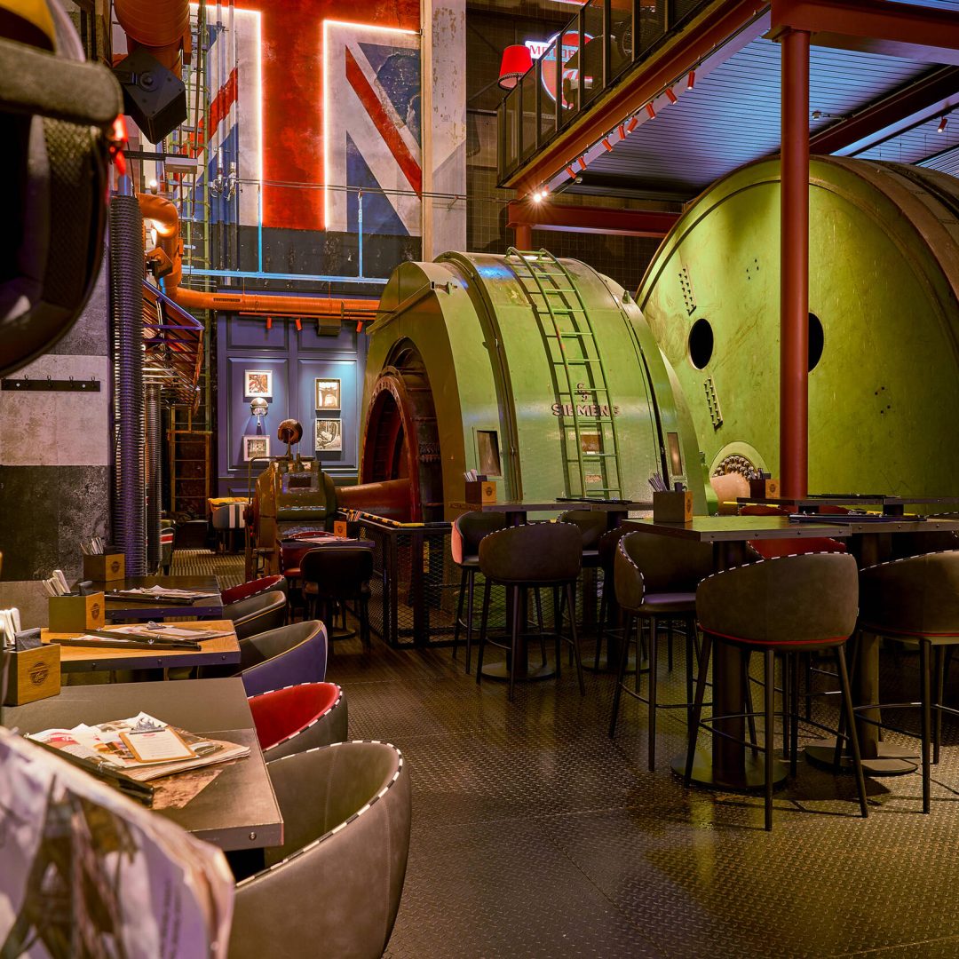 Industriedesign-Restaurant mit großen grünen Maschinengehäusen, Tischen und Stühlen unter Metallträgern