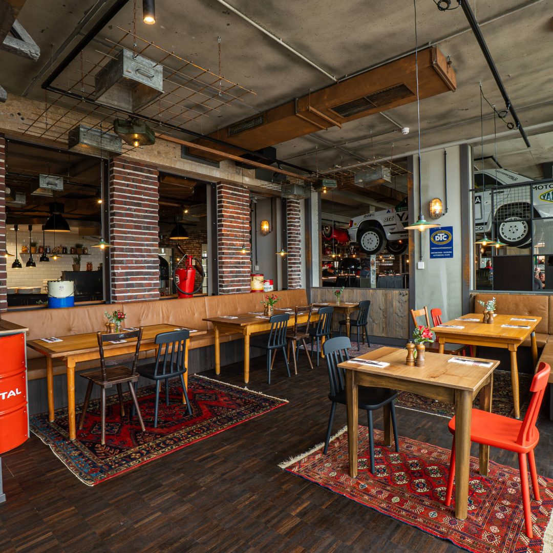 Industriell gestaltetes Restaurant mit Holztischen, roten Teppichen, Backsteinwänden und Auto-Dekor